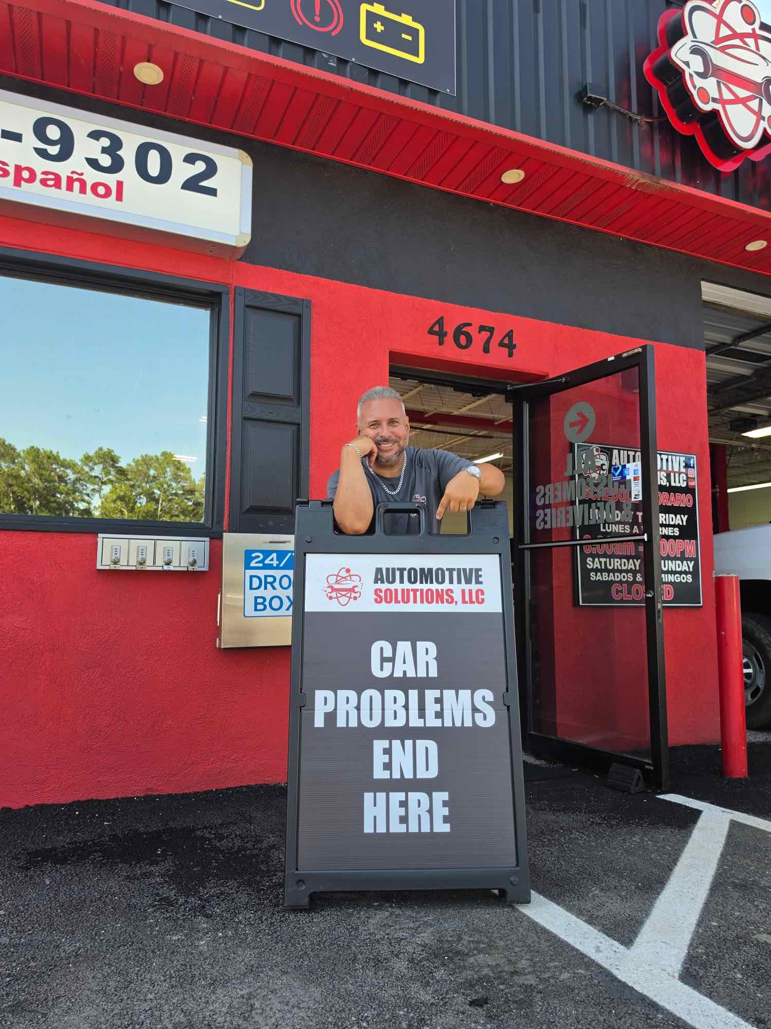 Aldo at the front door of Automotive Solutions with the sign that reads Car Problems End Here
