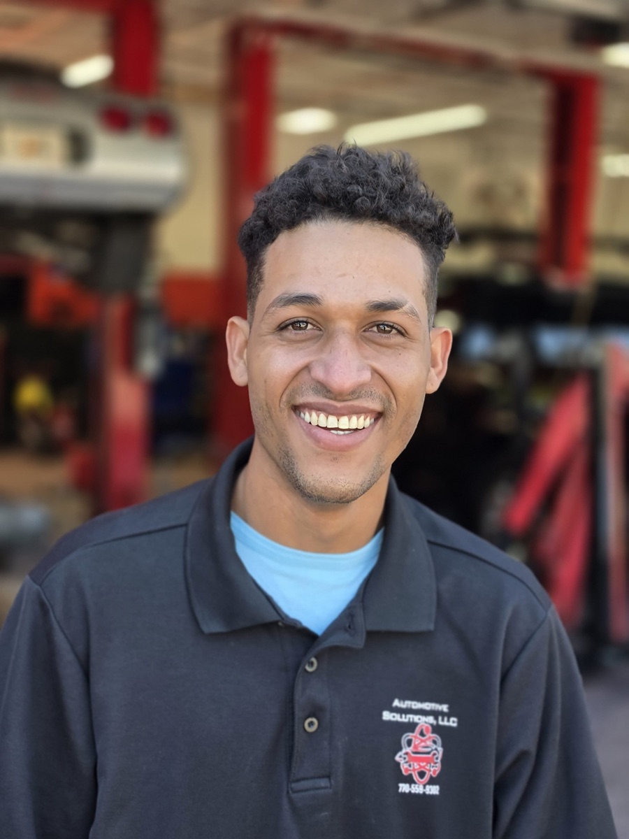 A body shop technician at Automotive Solutions, smiling in front of the service bays
