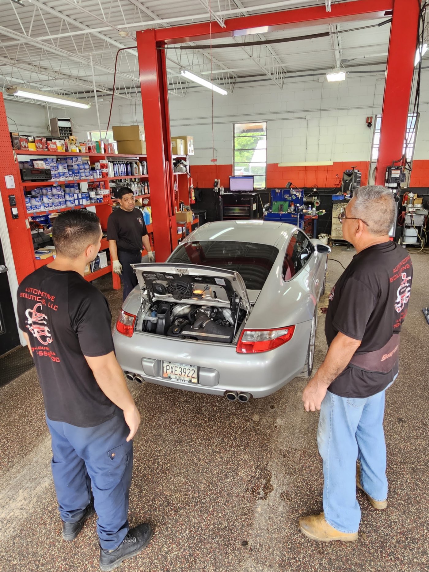 Three Automotive Solutions technicians around a Porsche on the lift inside the service bay
